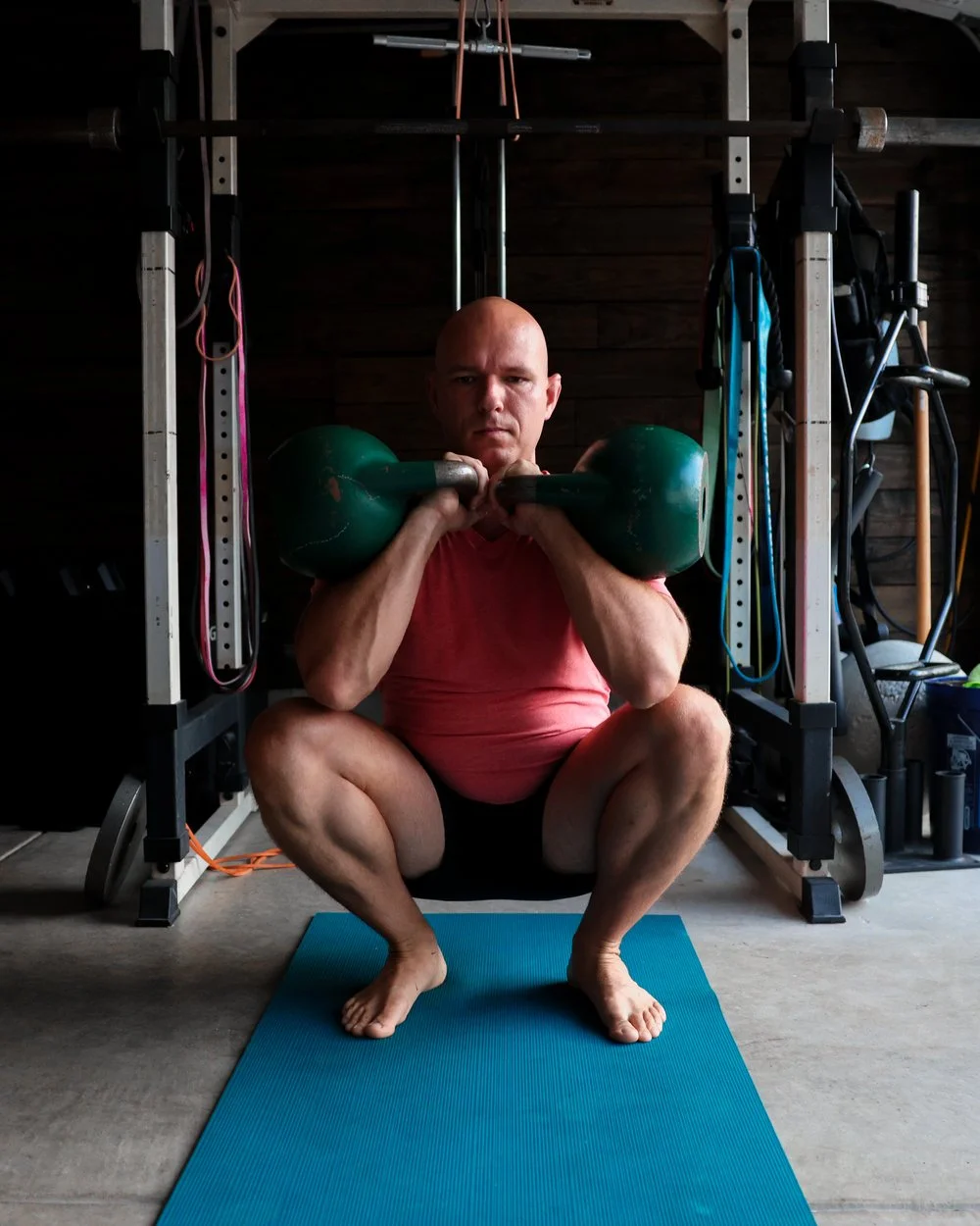 Anthoney holding two kettlebells in a deep squat in his training space